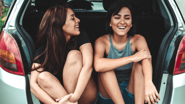Two females in back of car smiling and laughing
